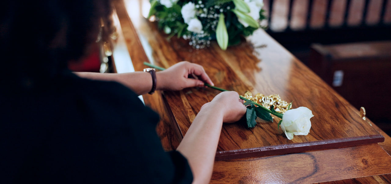 woman laying white rose on coffin